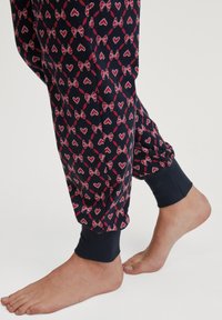 Marineblauwe broek met een herhaald patroon van roze strikken en harten, afgewerkt met geribde boorden en een zachte, gestructureerde stof.