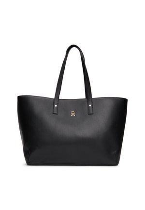 Sac cabas en cuir noir avec double bandoulière et un petit emblème doré centré sous les poignées sur fond blanc.