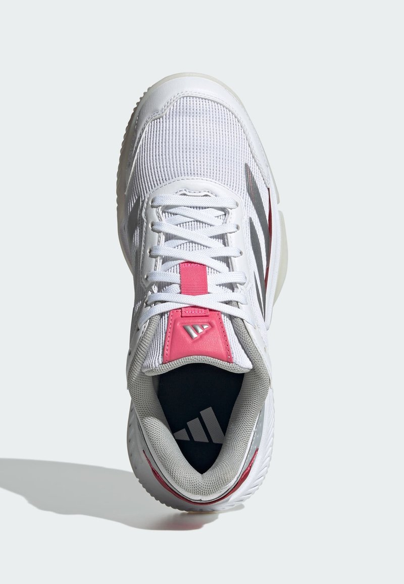 Zapatilla deportiva blanca con parte superior de malla, acentos rosas en la lengüeta y el interior gris. Presenta tres rayas negras y suela texturizada.