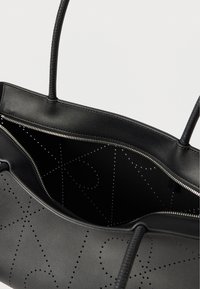 Μαύρη δερμάτινη τσάντα ώμου με διάτρητο γεωμετρικό μοτίβο, διπλές λαβές και μερικώς ανοιχτό ασημένιο φερμουάρ που αποκαλύπτει το εσωτερικό.