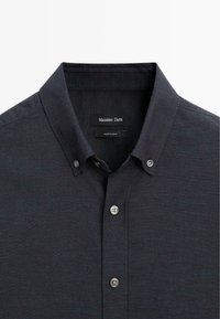 Camicia blu scuro con colletto classico, dotata di due bottoni al collo e di un'etichetta all'interno, realizzata in un tessuto testurizzato.