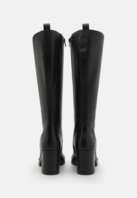 Bottes noires en cuir montantes jusqu'aux genoux avec une texture lisse, fermeture éclair, talon épais, détails de couture et boucles pour les enfiler.