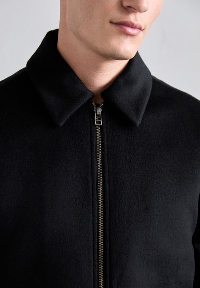 Black, textured jacket with a prominent collar and silver zipper. Designed with a fitted silhouette, showcasing a smooth fabric finish.
