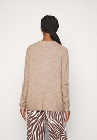Hellbrauner, strukturierter Pullover mit langen Ärmeln und rundem Ausschnitt, getragen mit braun-weißen, zebra gestreiften Hosen.
