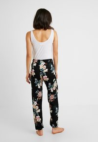 Florale zwarte pyjamabroek met een elastische tailleband, voorzien van grote roze en blauwe bloemen. Draag het met een getailleerd wit tanktop.