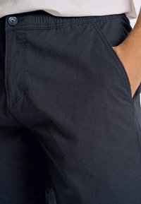 Mörkgrå shorts i ett texturerat, lättviktigt tyg. Har en enkel knappstängning och sidofickor. Söm detaljer syns.