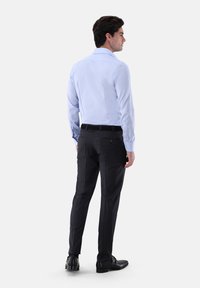 Hellblaues Langarmhemd kombiniert mit schwarzer Anzughose. Das Hemd hat einen klassischen Kragen; die Hose ist schmal geschnitten und hat eine glatte Textur.