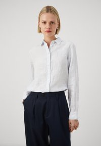 Jasnoniebieska i biała w paski koszula z guzikami, z kołnierzykiem, długimi rękawami i luźnym krojem, w połączeniu z ciemnoniebieskimi spodniami o wysokim stanie.