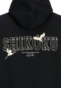 Sudadera negra con capucha que presenta "SHIKOKU" en una fuente gruesa. Ilustraciones de dos grúas en vuelo. El texto incluye una descripción de Shikoku, Japón.