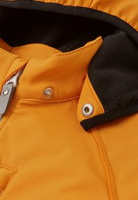 Section de veste d'extérieur orange avec une doublure en polaire noire, un bouton-pression et des coutures contrastantes le long de la zone de la fermeture éclair.