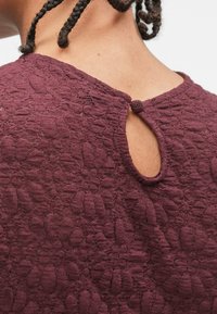 Top bordeaux con un motivo floreale testurizzato, scollatura rotonda e un dettaglio a occhiello sulla schiena con chiusura a loop in tessuto.