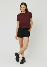 T-shirt courte maroon portée avec un short noir ajusté. Le modèle porte des chaussures à lacets noires avec des semelles épaisses et des chaussettes froncées bordeaux.