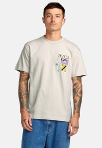 Lichtgrijs katoenen t-shirt met een ronde hals, voorzien van kleurrijke grafische patches en abstracte ontwerpen op de linkerkant van de borst.