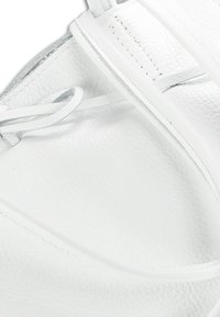 Chaussure en cuir blanc avec une surface texturée, dotée de lacets fins et d'un design épuré. Des détails de couture notables soulignent les bords.