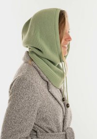 Groene geribbelde gebreide capuchon met verstelbare trekkoorden, gelaagd over een grijze textuurjasje, die een comfortabele, veelzijdige uitstraling heeft.