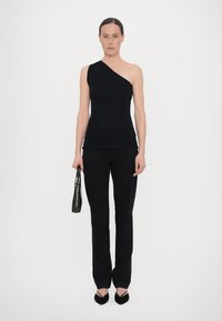 Zwarte geribbelde mouwloze top met een asymmetrische halslijn, gecombineerd met zwarte op maat gemaakte broek en een groene handtas met krokodillenpatroon.