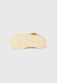 Sole of a shoe featuring a textured cream rubber bottom with traction patterns and brand logo embossed, showcasing durability and grip design.