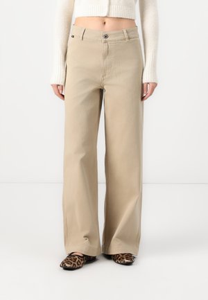 Beige wide-leg trousers with a button closure and front pockets, made of soft material, paired with leopard print shoes.