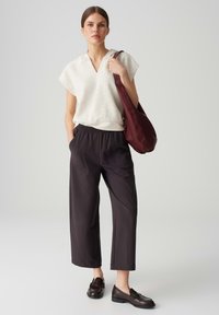 Cream, textured short-sleeve top; loose black trousers; dark shoes; carrying a maroon shoulder bag. Simple, casual outfit with a relaxed fit.
