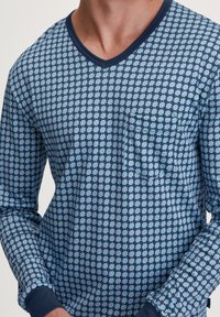 Lange mouwen V-hals shirt in lichtblauw met een donkerblauw geometrisch patroon. Voorzien van een zak en contrasterende donkerblauwe manchetten. Zachte stofstructuur.