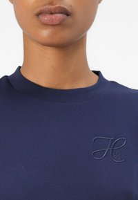 Sweatshirt bleumarin cu guler rotund, fabricat dintr-un material neted, având un logo embosat pe piept. Design simplu și minimal, fără modele.