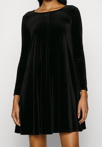 Zwarte fluwelen jurk met lange mouwen, ronde halslijn, A-lijn silhouet en een gladde textuur. Voorzien van minimalistische ontwerpelementen.