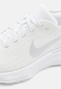 Witte sportschoen met een textuurbreisel bovenkant, synthetische accenten en een rubberen zool. Veters zijn door verstevigde oogjes geweven.