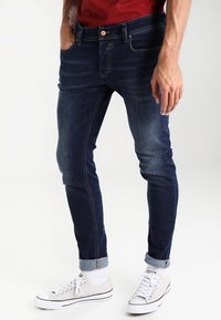 Mörkblå denimjeans med smal passform, utrustade med en urblekt tvätt, framfickor och uppvikta ben, kombinerade med vita sneakers och strumpor.