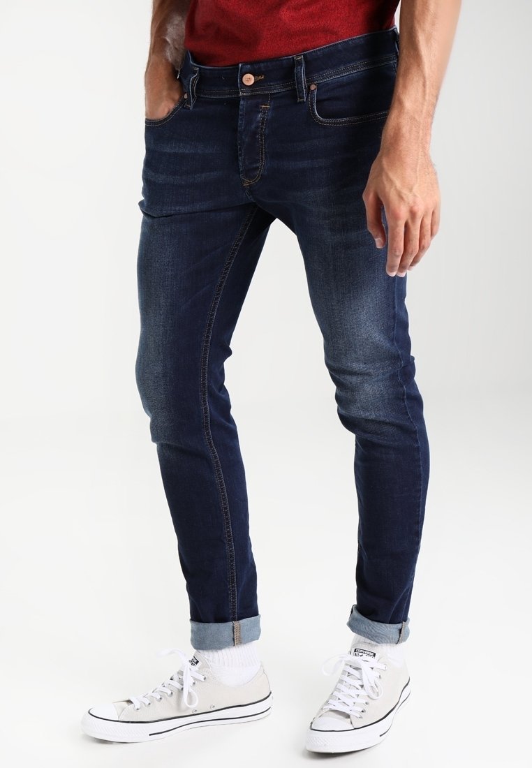 Mörkblå denimjeans med smal passform, utrustade med en urblekt tvätt, framfickor och uppvikta ben, kombinerade med vita sneakers och strumpor.