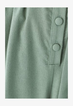 Tejido verde claro con una textura entrelazada, con una tapeta y dos grandes botones redondos del mismo color.