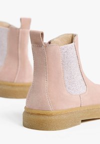 Stivaletti alla caviglia in suede rosa con pannelli elastici ai lati, dettagli in tessuto testurizzato e suole in gomma. Presentano un pratico tassello sul retro per una facile calzata.