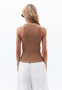 Top corto a coste marrone con un design aderente e spalline larghe, abbinato a pantaloni a gamba larga di colore chiaro.