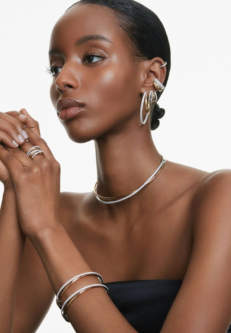 Silber- und Goldmetallschmuck getragen; umfasst Creolen, eine Choker-Halskette und gestapelte Armbänder mit funkelnden Akzenten und glatten Texturen.