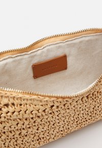 Woven natural straw pouch with a gold zipper, beige fabric lining, and a leather tag inside. Textured exterior with intricate weave pattern.
