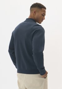 Marinblå lätt sweatshirt med krage, ribbade mudd och nederkant; tillverkad av ett mjukt, strukturerat material. Bakifrån visar den en slät skräddarsydd design.