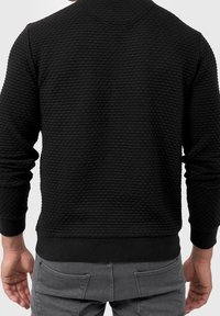 Zwart gestructureerd sweatshirt met een geweven patroon, geribde boorden en onderrand, met een ronde hals en een comfortabele pasvorm.