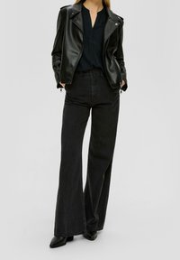 Giacca biker in pelle nera, pantaloni flare in denim scuro e stivaletti neri alla caviglia. Texture liscia con zip sulle tasche e vestibilità elegante.