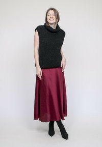 Gilet à col roulé en tricot noir associé à une jupe satin bourgogne fluide et des bottes noires à talons. Texture douce, coupe décontractée et design élégant.