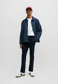 Navy blue linen jacket with buttons, white t-shirt with text, navy pants, and white sneakers with black accents and a tan sole. Red cap.
