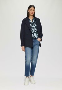 Manteau bleu marine croisé sur un haut à motifs bleu et blanc, associé à un jean bleu clair et des baskets blanches. Vue à plat, sans détails supplémentaires.