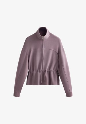 Orvokkivioletti pitkähihainen vetoketjullinen takki, jossa on pystypääntie ja säädettävä kiristysnauha vyötäröllä, valkoisella taustalla.