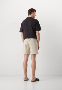 Cămașă neagră cu mânecă scurtă și pantaloni scurți bej cu talie elastică, asortați cu sandale închise la culoare. Design simplu, material din bumbac, croi relaxat.