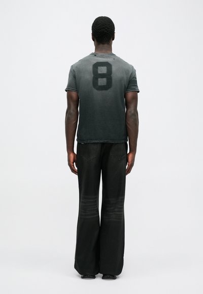 Dunkelgraues T-Shirt mit einer großen schwarzen "8" auf dem Rücken, kombiniert mit weit geschnittenen schwarzen Hosen, die beide eine strukturierte Oberfläche haben.