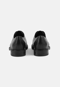 Black leather shoes with a smooth texture, rounded backs, and flat soles. Minimalistic design with no visible hardware or patterns.