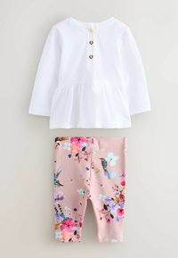 Hvid langærmet top med peplumkant og hjerteformede knapper, kombineret med lyserøde leggings med livlige blomster- og fuglemønstre.