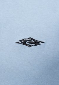 Μαύρο κεντημένο αφηρημένο λογότυπο σε φωτεινό γαλάζιο υφασμάτινο φόντο με υφή.