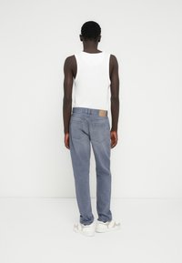 Ανοιχτό μπλε τζιν παντελόνι με ίσια εφαρμογή, που διαθέτει δύο πίσω τσέπες και ένα καφέ δερμάτινο ταμπελάκι στη μέση. Συνδυασμένο με λευκή αμάνικη μπλούζα.