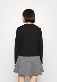 Fekete, hosszú ujjú felső, kerek nyakkivágással, fekete-fehér kockás, bő szoknyával párosítva. Simogatós tapintás, laza dizájn.