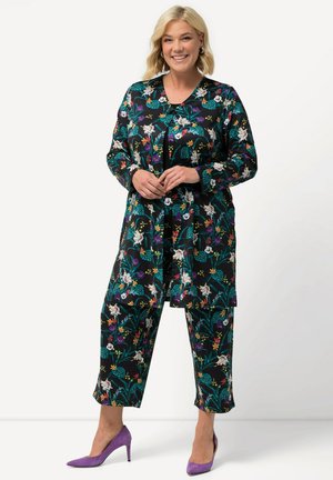 Tenue à motifs floraux avec une base noire, des couleurs vives, des manches longues et un pantalon court ; associée à des talons hauts violets.