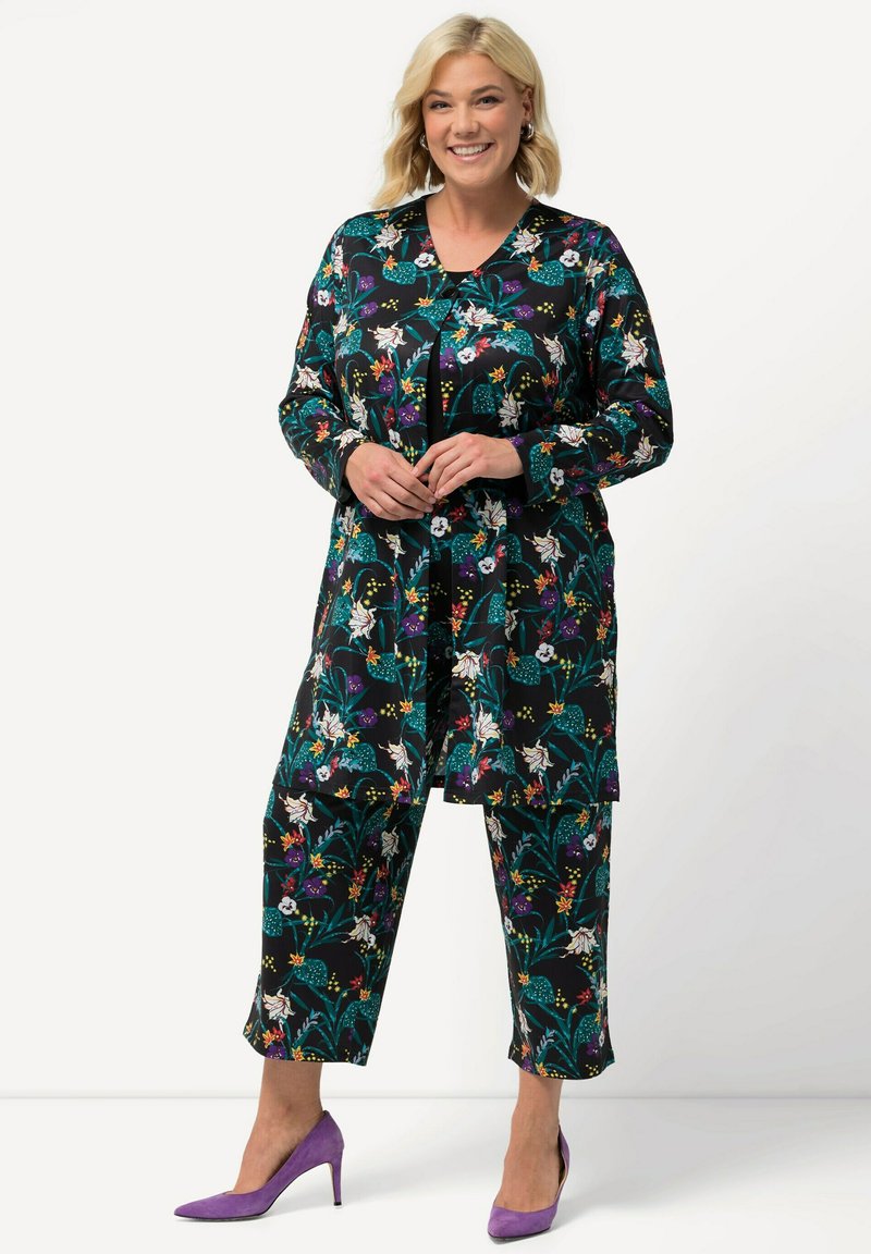 Květinový outfit s černým základem, živými barvami, dlouhými rukávy a zkrácenými kalhotami; v kombinaci s fialovými vysokými podpatky.